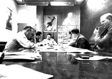 Le groupe du projet Sign dans la salle de conférence du département T-2 à Wright Patterson, en 1948. A partir de la cauche et de la table on trouve : le lieutenant-colonel Malcolm Seashore, chef de l'Analyse Technique du Renseignement du Commandement du Matériel, une personne non-identifiable masquée par Seashore, le lieutenant-colonel J. J. Hausman, Howard McCoy ; [ce qu'on pense être] le capitaine Robert Sneider, Officier de Projet sous McCoy et Clingerman, [ce qu'on pense être] le colonel William Clingerman, officier executif pour l'Analyse du Renseignement du Commandement du Matériel (MCIA) et John 'Red' Honaker, liaison avec Twining, tenant sa pipe